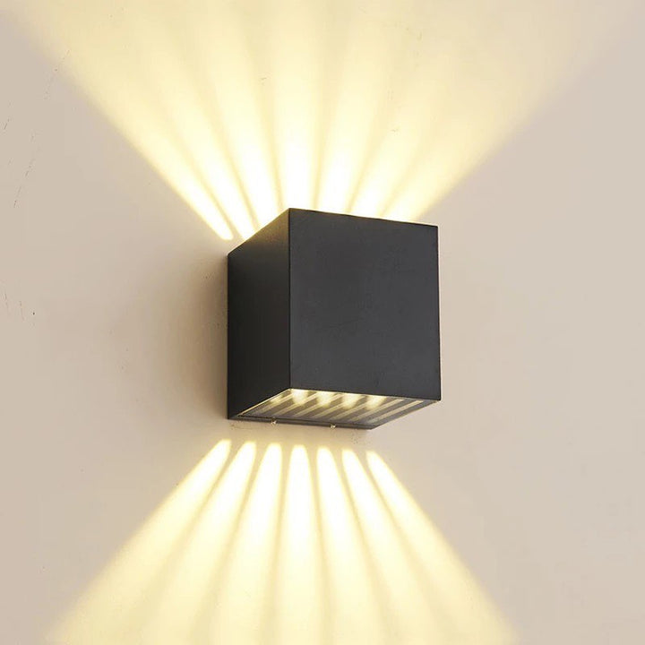 A modern LED outdoor wall light with a dual beam effect, showing a sleek black cube design and emitting light from the top.