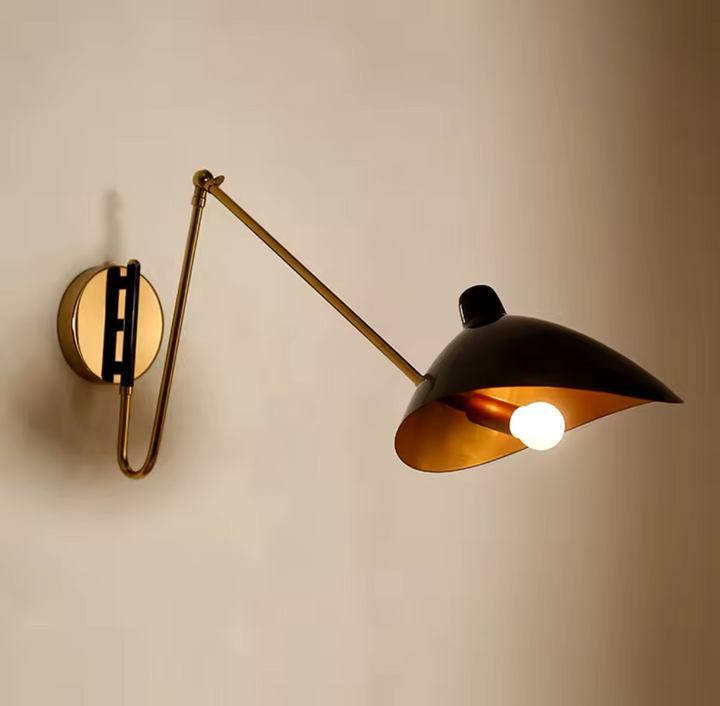 A modern adjustable bedside wall lamp with a brass finish, featuring an adjustable arm and a circular brass base, mounted on a wall.