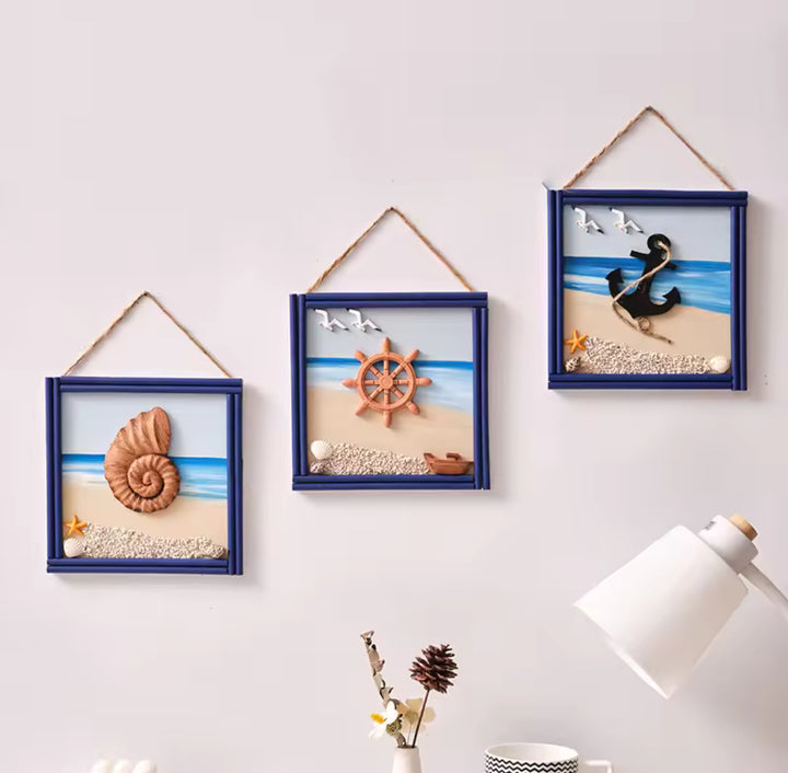 Set of three square nautical wall art frames featuring a shell, ship wheel, and anchor on a beach background