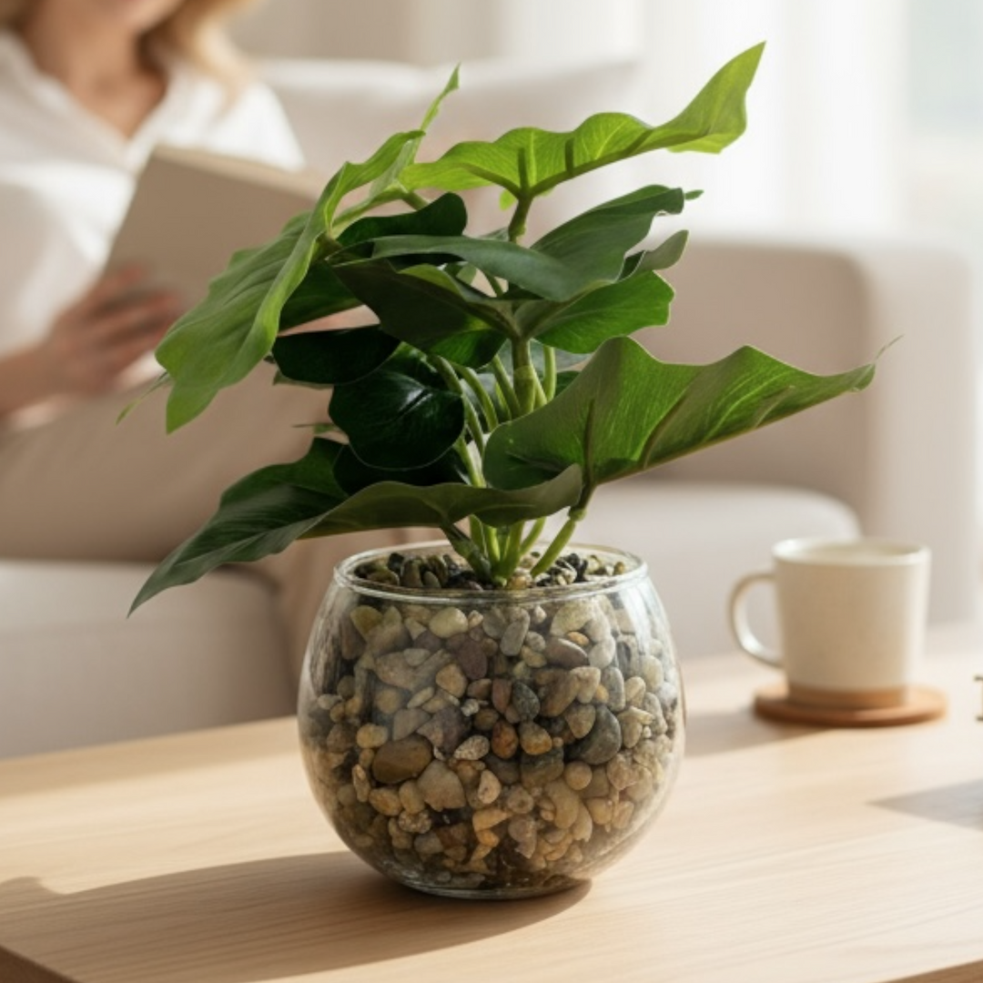 Artificial green plant in glass vase with pebbles on wooden table
