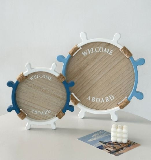 Nautical-themed decorative wooden trays shaped like ship wheels with “Welcome Aboard” text, in blue and white.