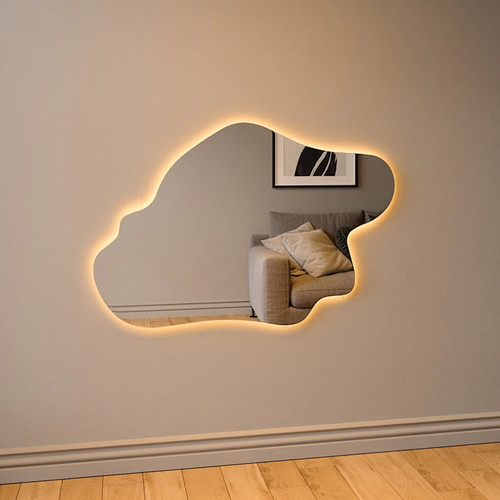 Abstract island-shaped LED mirror with warm backlighting mounted on a beige wall above a wooden floor in a modern living room