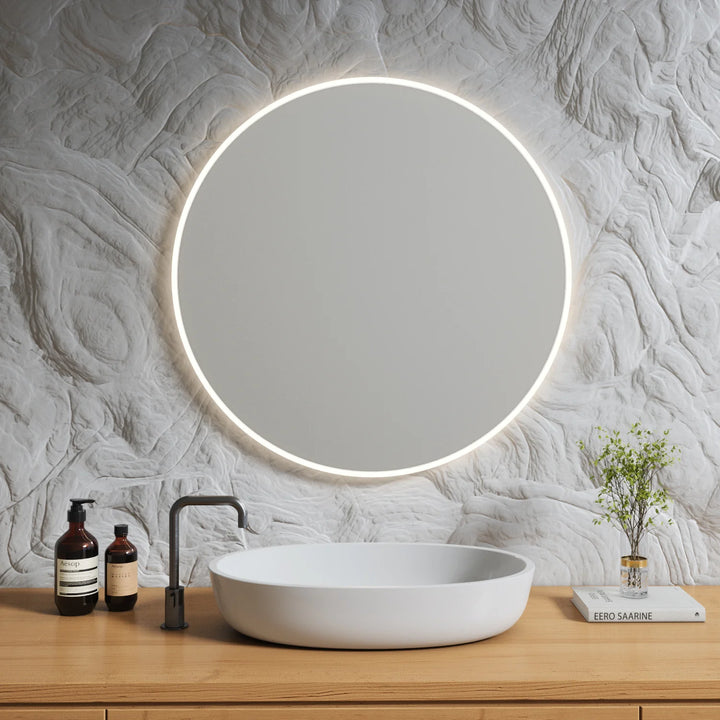 Minimalist round LED mirror mounted on a sculptural wall above a wood vanity with a modern vessel sink