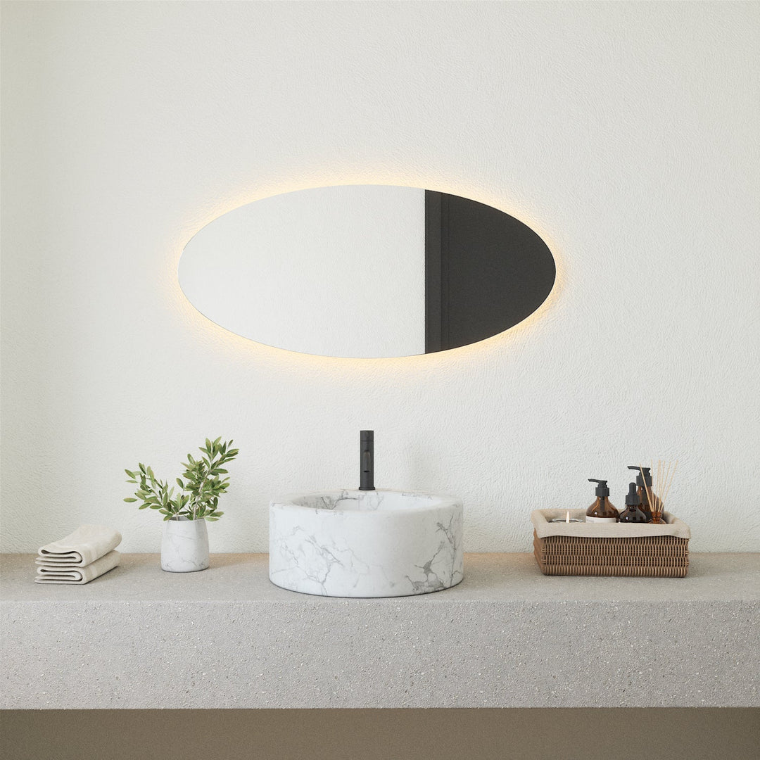 Frameless oval LED mirror with warm backlight mounted above a marble basin