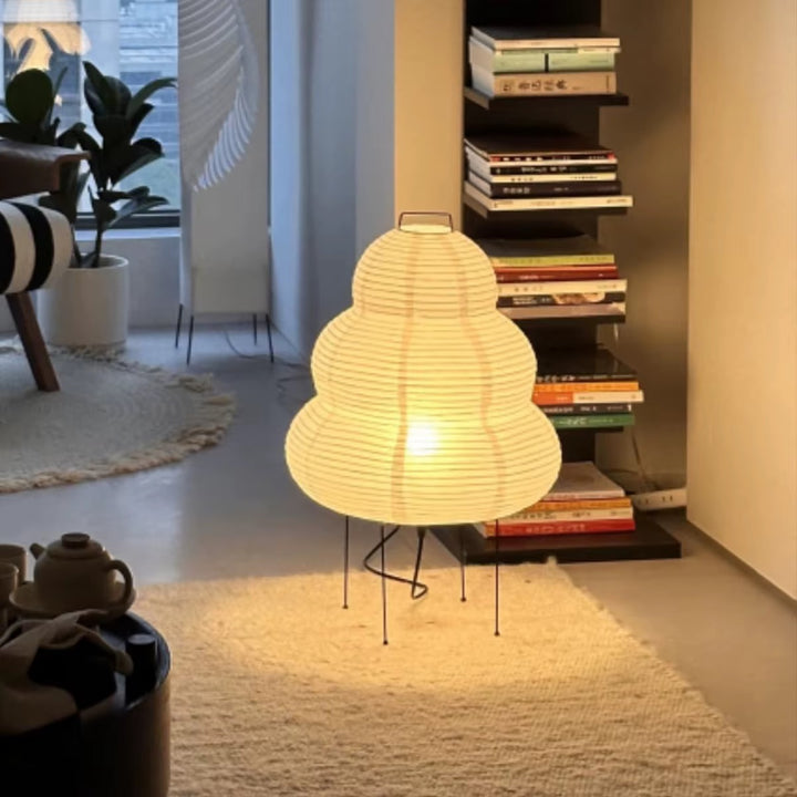 Sculptural warm white paper lantern floor lamp with a rounded layered shade and black metal legs in a modern living room