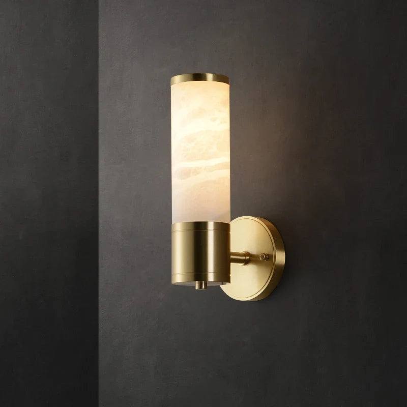 Brass wall sconce with a cylindrical cream alabaster-style shade mounted on a dark wall