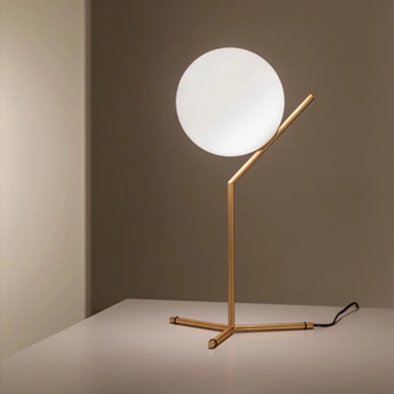 A modern brass and globe table lamp with a frosted glass globe and a gold-colored base, positioned on a table against a neutral background.