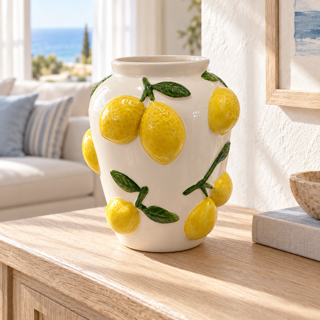 Ivory ceramic vase decorated with raised yellow lemons and green leaves on a light wood console table