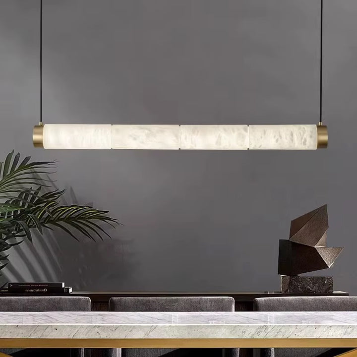 Modern linear alabaster pendant light with brass end caps suspended above a contemporary console table