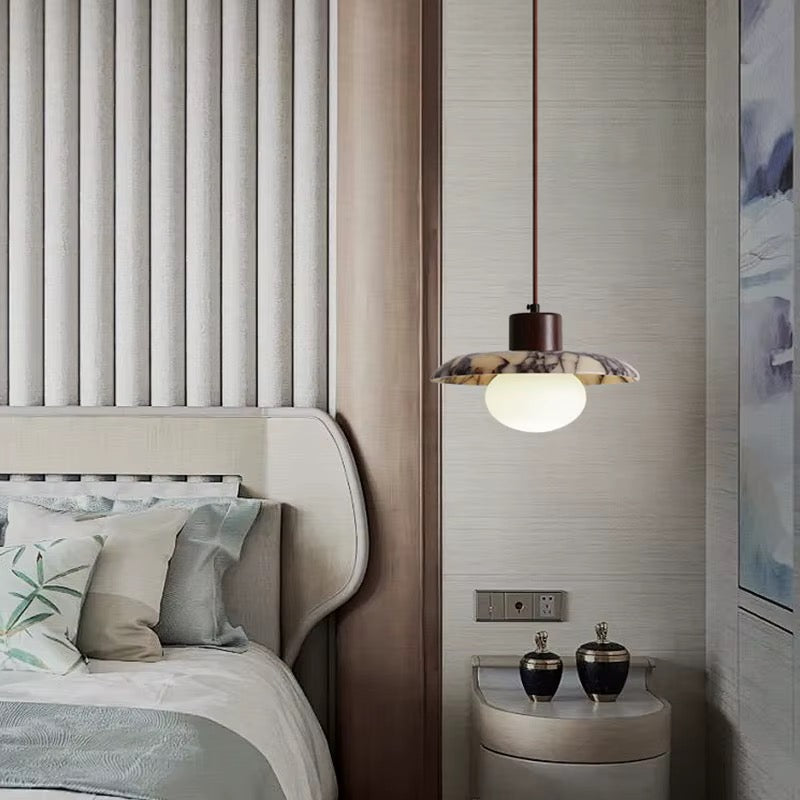 Modern opal globe pendant light with a dark metal stem beside a bedroom bed