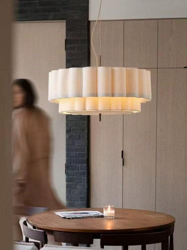 Modern layered pleated pendant light with a wide circular white shade and warm diffused illumination above a dining table.