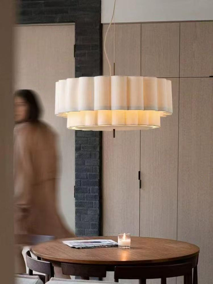 Modern layered pleated pendant light with a wide circular white shade and warm diffused illumination above a dining table.