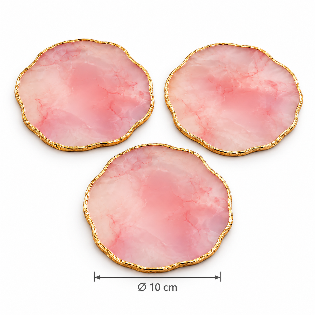Three pink, stone-look coasters with gold-tone edges arranged on a light wood coffee table, with a drinking glass resting on one coaster.