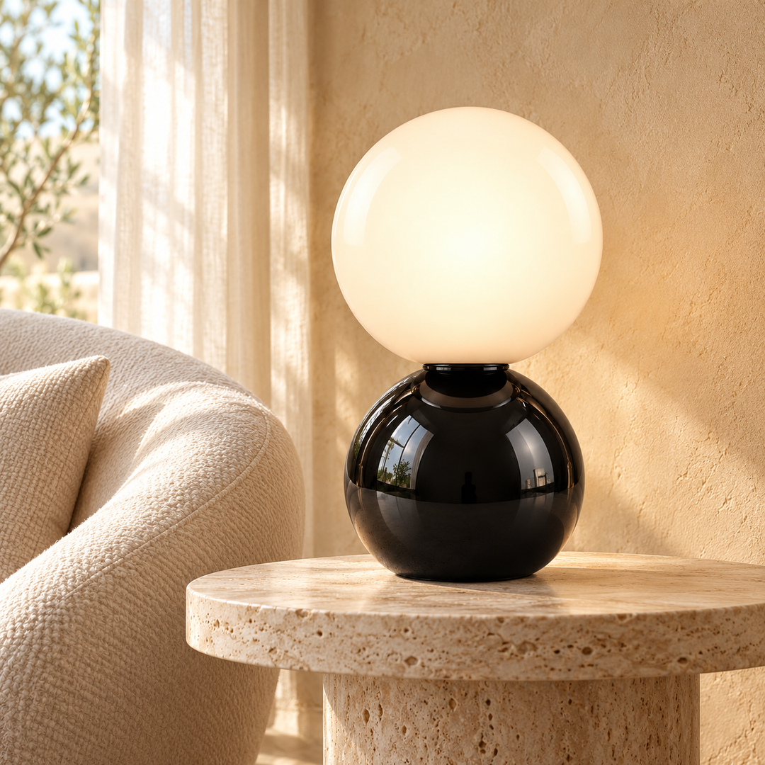 Table lamp with a glossy black spherical base and glowing opal globe shade on a stone side table