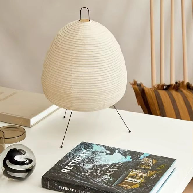 Round warm white paper lantern table lamp with a pleated shade and slim black legs on a desk