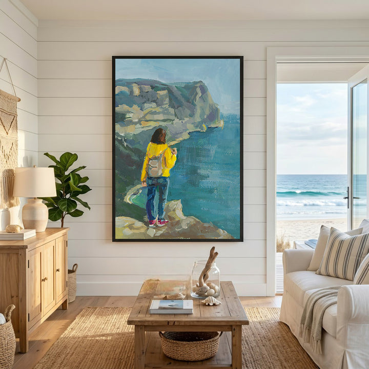 Wadi Home Coastal Cliffside Vista painting featuring a woman in a yellow jacket looking at the ocean.
