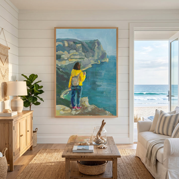 Wadi Home Coastal Cliffside Vista painting featuring a person in a yellow jacket looking at the ocean.