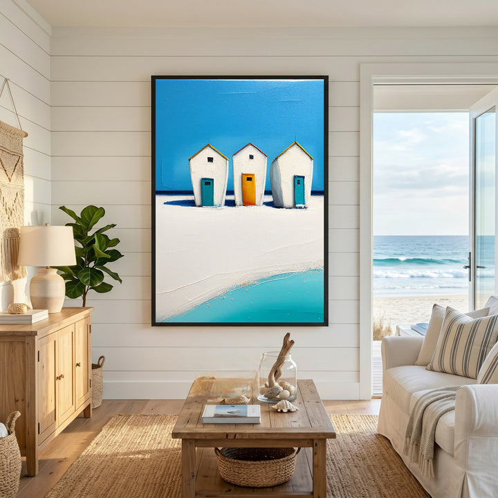 Wadi Home painting of three white beach huts with blue and orange doors on a sandy beach with turquoise water and blue sky.