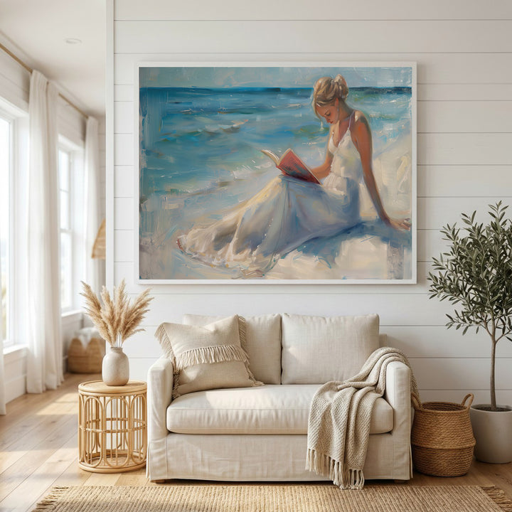 Wadi Home canvas art of a woman in a white dress reading a book on a serene beach with blue ocean waves.