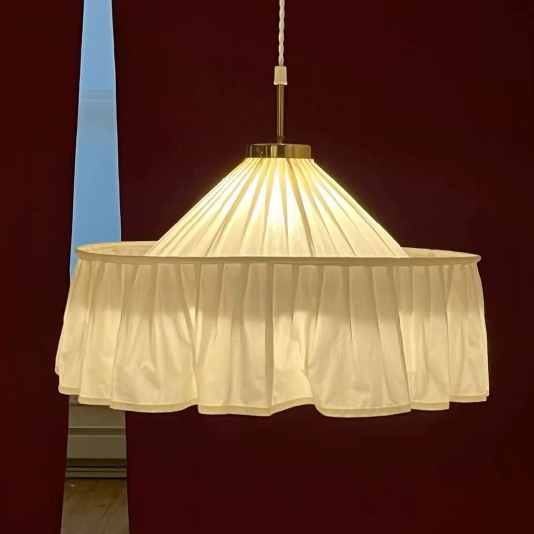 Cream pleated fabric pendant light with a gathered scalloped shade hanging against a dark red wall