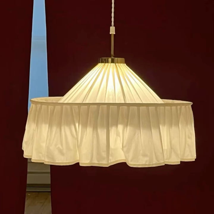 Cream pleated fabric pendant light with a gathered scalloped shade hanging against a dark red wall