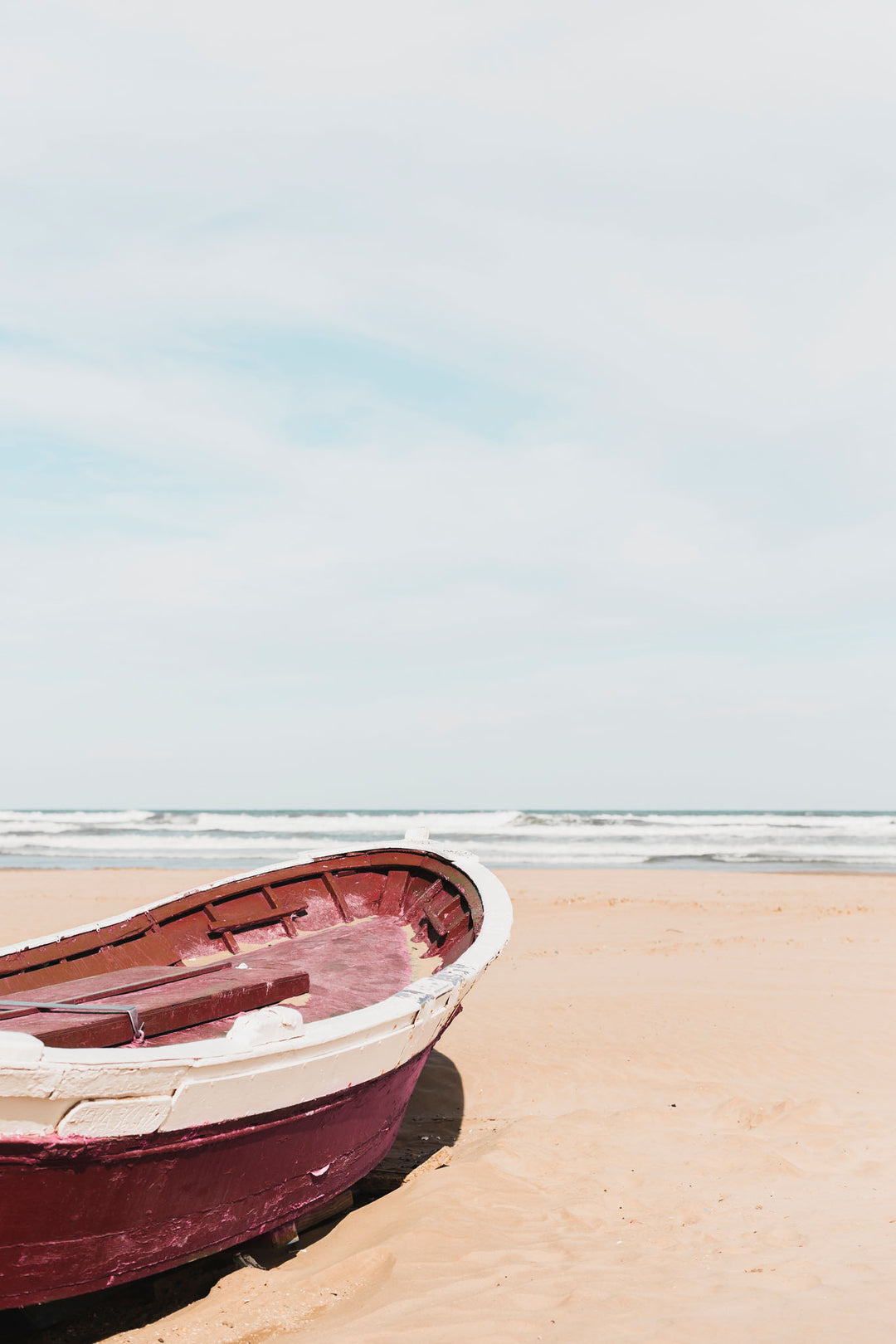 Wadi Home coastal wall art featuring a deep red boat on a sandy beach, displayed in a bright, modern living room.