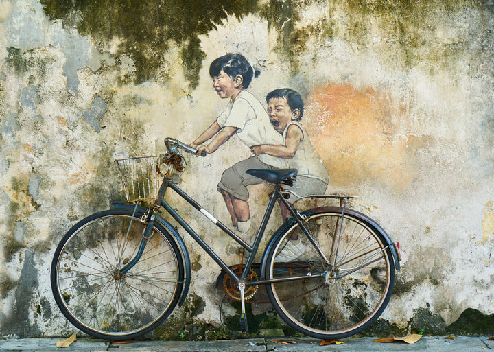 Wadi Home wall art print of two children riding a vintage bicycle against a weathered, textured urban wall.