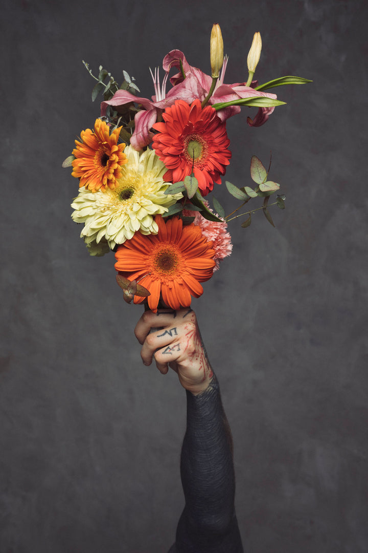 Wadi Home framed wall art featuring a tattooed hand holding a vibrant floral bouquet against a dark grey background.