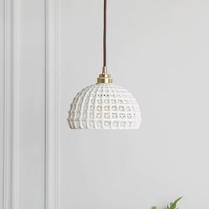 White dome pendant light with an open lattice shade and brass-toned fitting, hanging against a light wall