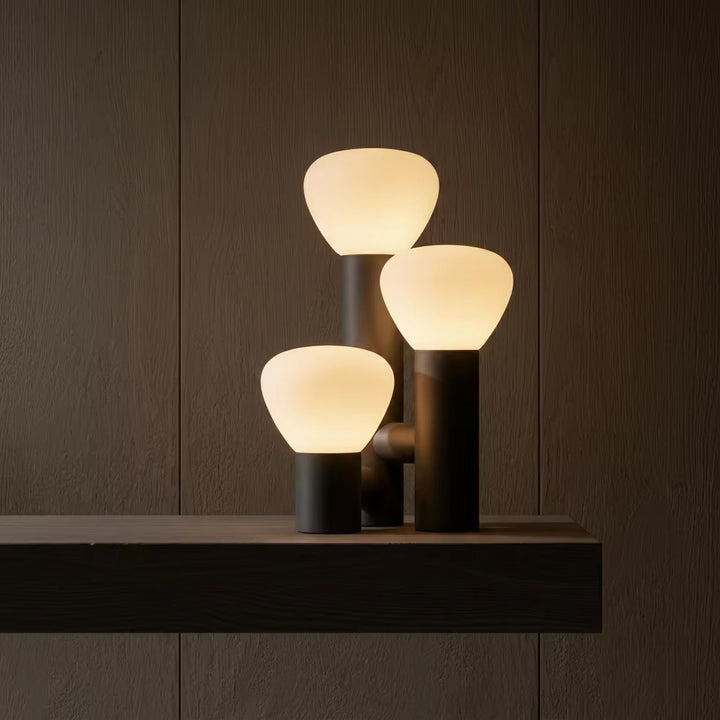 Sculptural table lamp with three glowing cream-colored globes at staggered heights on a dark base