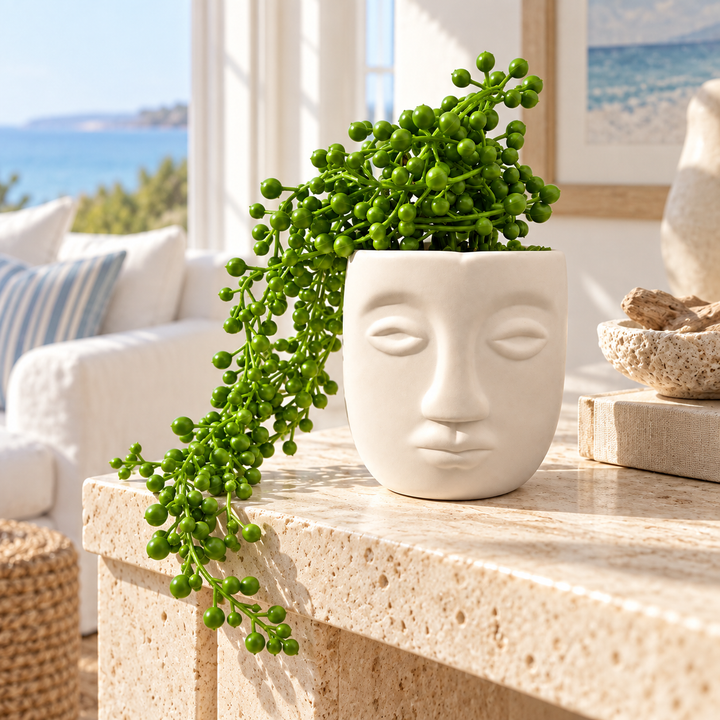 White ceramic face planter with cascading artificial green string-of-pearls plant on a modern living room table