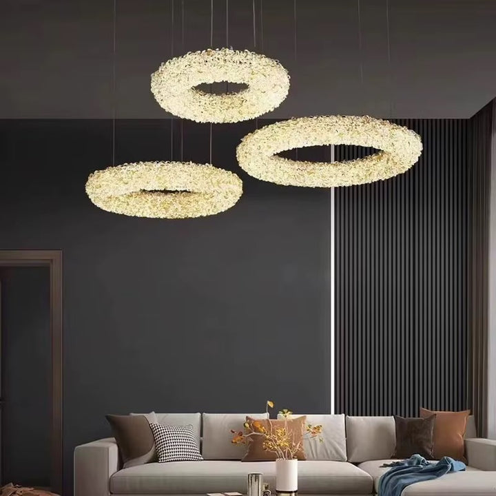Three textured gold-toned ring pendant lights suspended at different heights in a modern living room