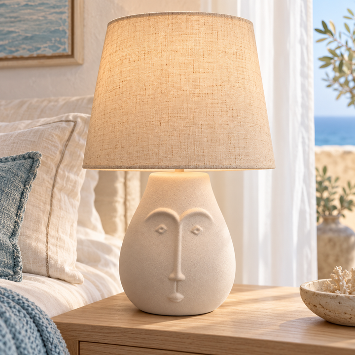 Beige ceramic face table lamp with a natural linen shade on a bedroom nightstand
