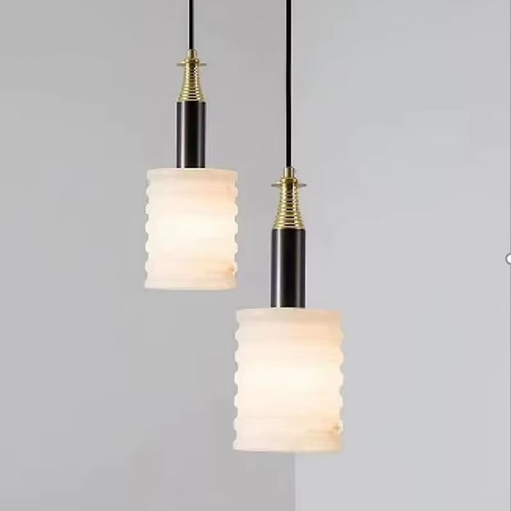 Pair of ribbed ivory pendant lights with black stems and brass fittings suspended from a ceiling