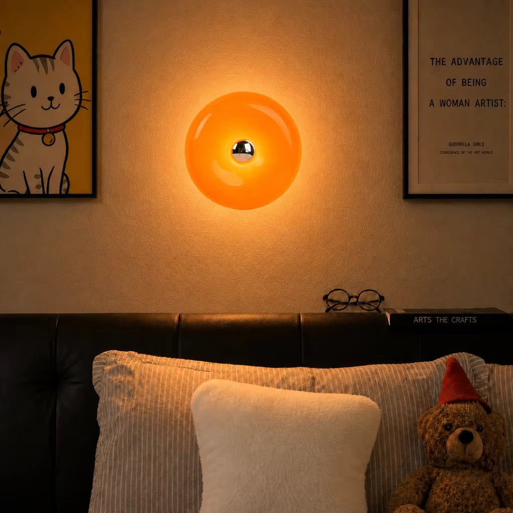 Glowing glossy orange round wall light above a bed, with a small metallic center