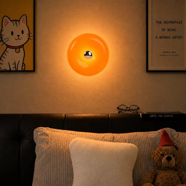 Glowing glossy orange round wall light above a bed, with a small metallic center