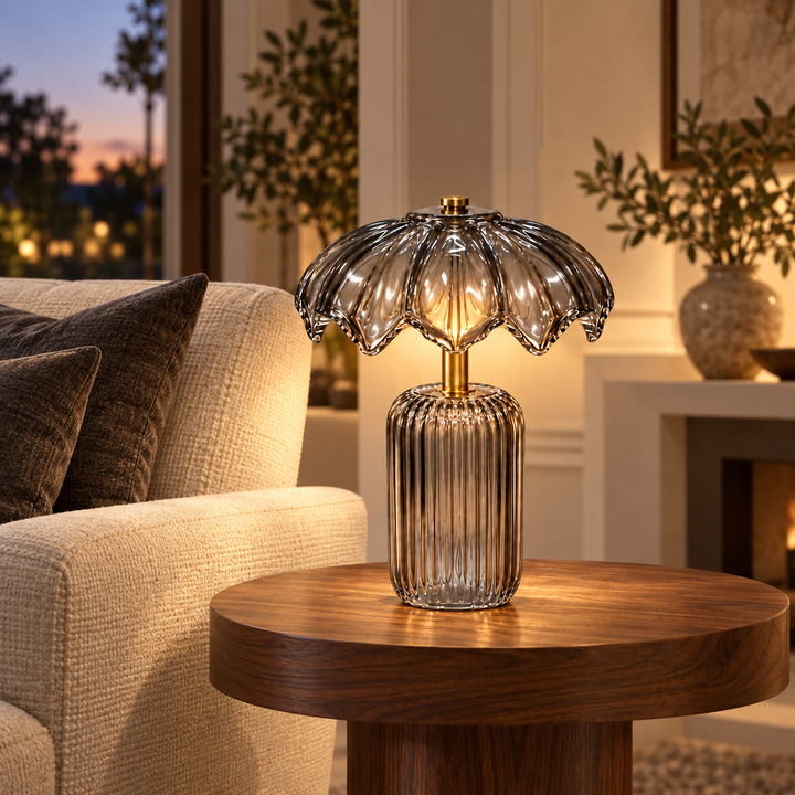 Illuminated table lamp with a ribbed smoked-glass base, scalloped shade and gold-tone accents on a wooden side table.
