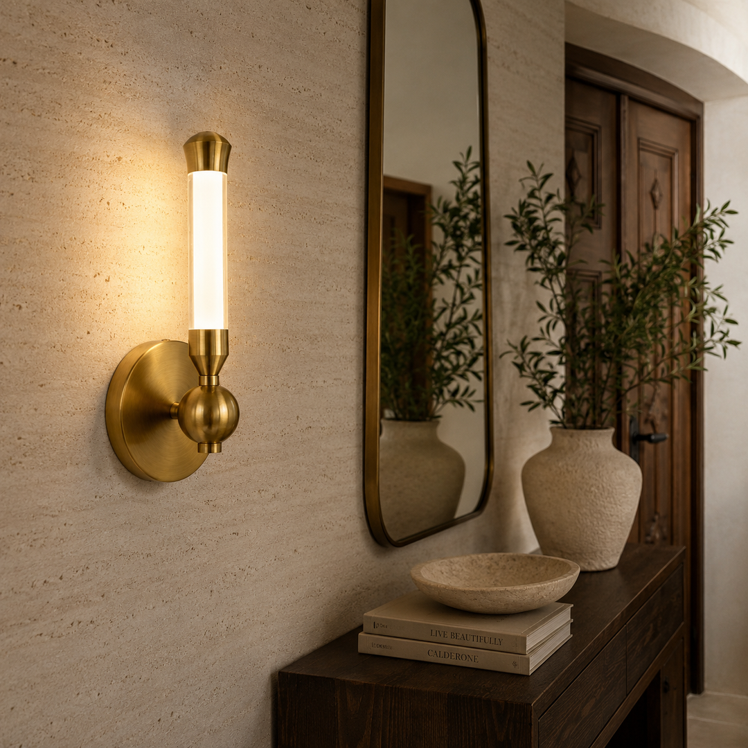 Modern brushed brass wall sconce with a spherical accent and vertical opal glass diffuser, mounted on a textured hallway wall.