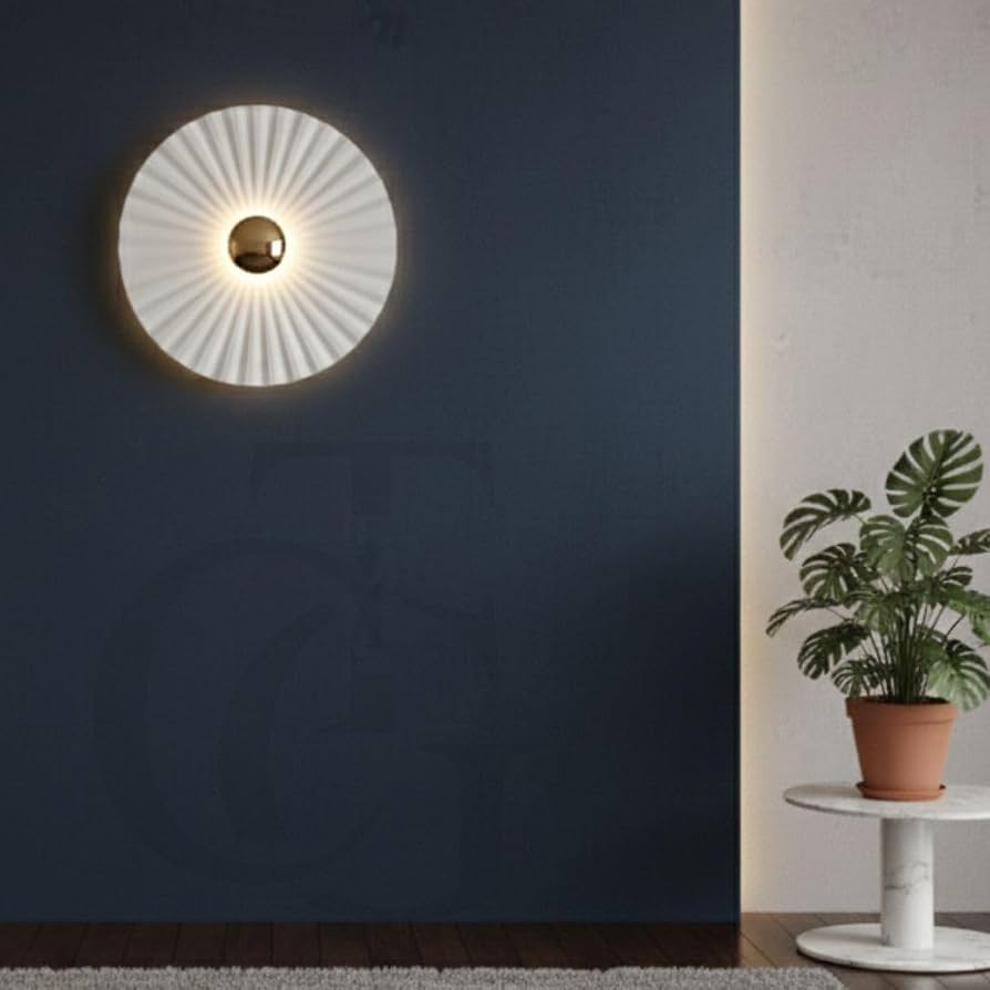 Round white pleated wall sconce glowing on a dark blue wall beside a potted plant