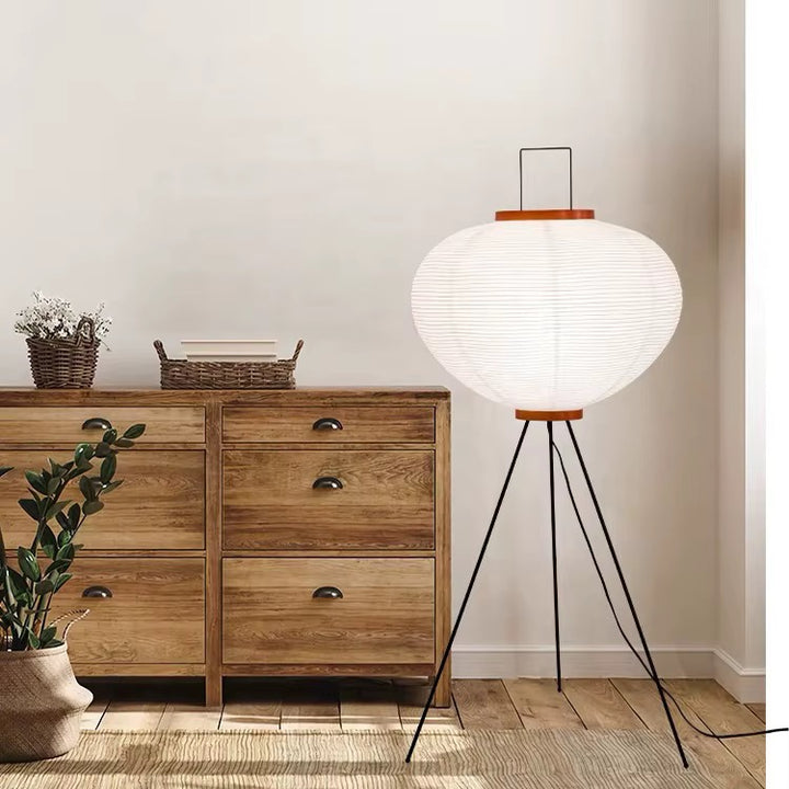 White paper lantern tripod floor lamp with black legs and wooden accents beside a wooden sideboard