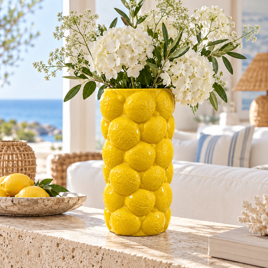 Tall bright yellow vase with a raised lemon-like texture, holding white flowers and greenery on a stone console.