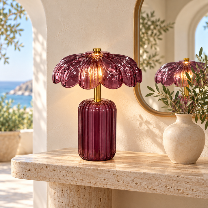 Burgundy glass table lamp with a ribbed base, flower-shaped shade and gold-tone stem, illuminated on a console table.