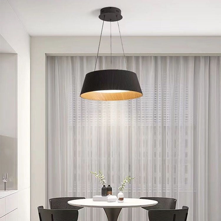 Black pleated drum pendant light with a warm wood-toned interior hanging above a modern dining table