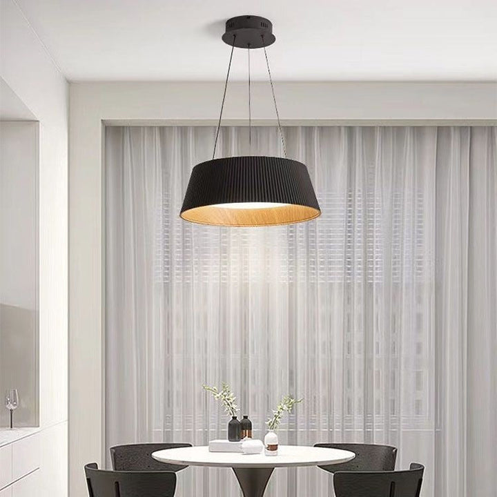 Black pleated drum pendant light with a warm wood-toned interior hanging above a modern dining table