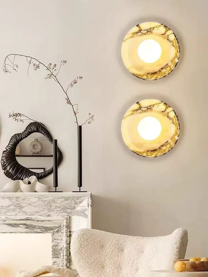 Two round wall lights with glowing centers and cream-and-amber marbled surrounds, mounted above a fireplace in a neutral living room.