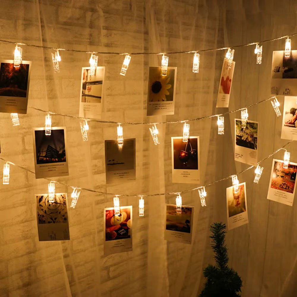 Warm white string lights with clips holding photographs on an indoor wall