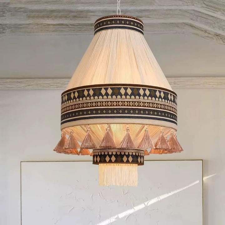 Hanging pendant light with a pleated cream shade, dark geometric trim, and peach-toned tassel fringe