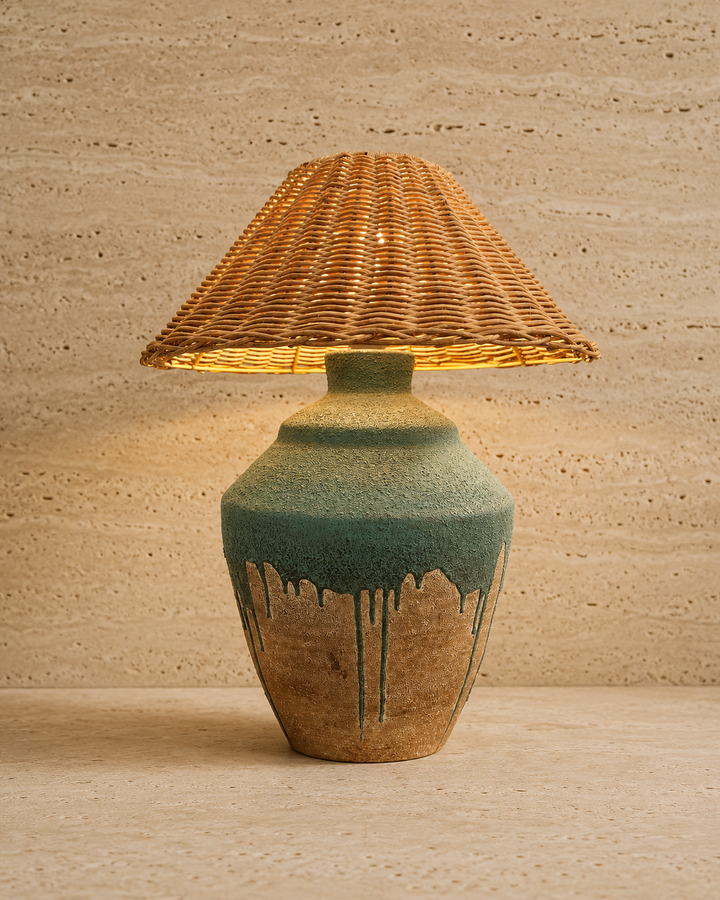 Rustic table lamp with a woven rattan shade and textured earthy ceramic base, emitting warm ambient light