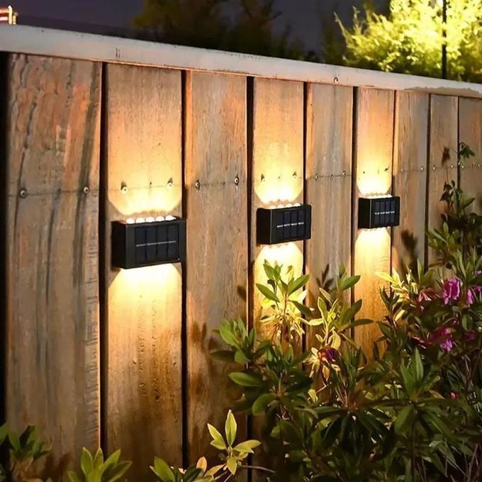 Black outdoor lights mounted on a wooden garden fence, casting warm light upward and downward