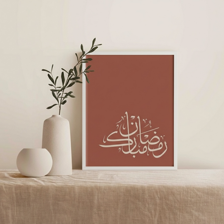 Framed artwork with Arabic calligraphy on a red background, placed on a wooden surface with decorative vases.